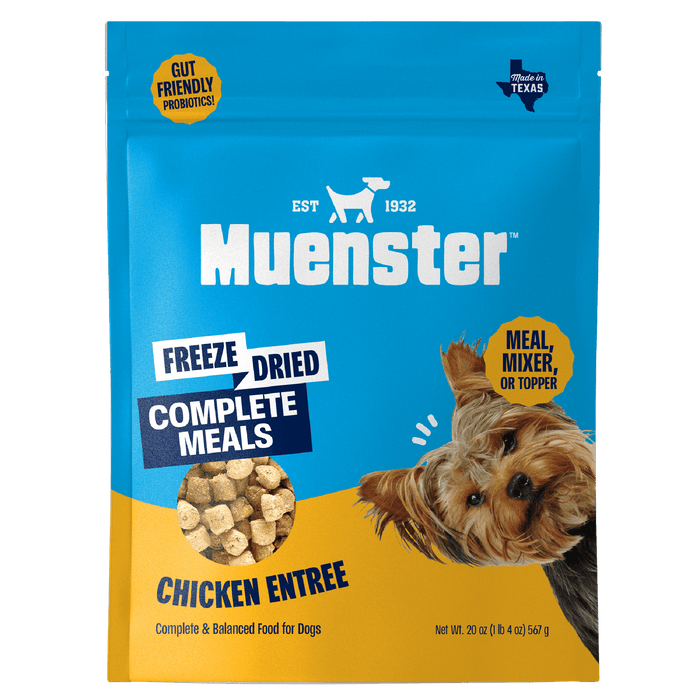 A blue and yellow Muenster dog food bag features a small dog, freeze-dried chicken pieces, and text highlighting it as a complete meal or topper.