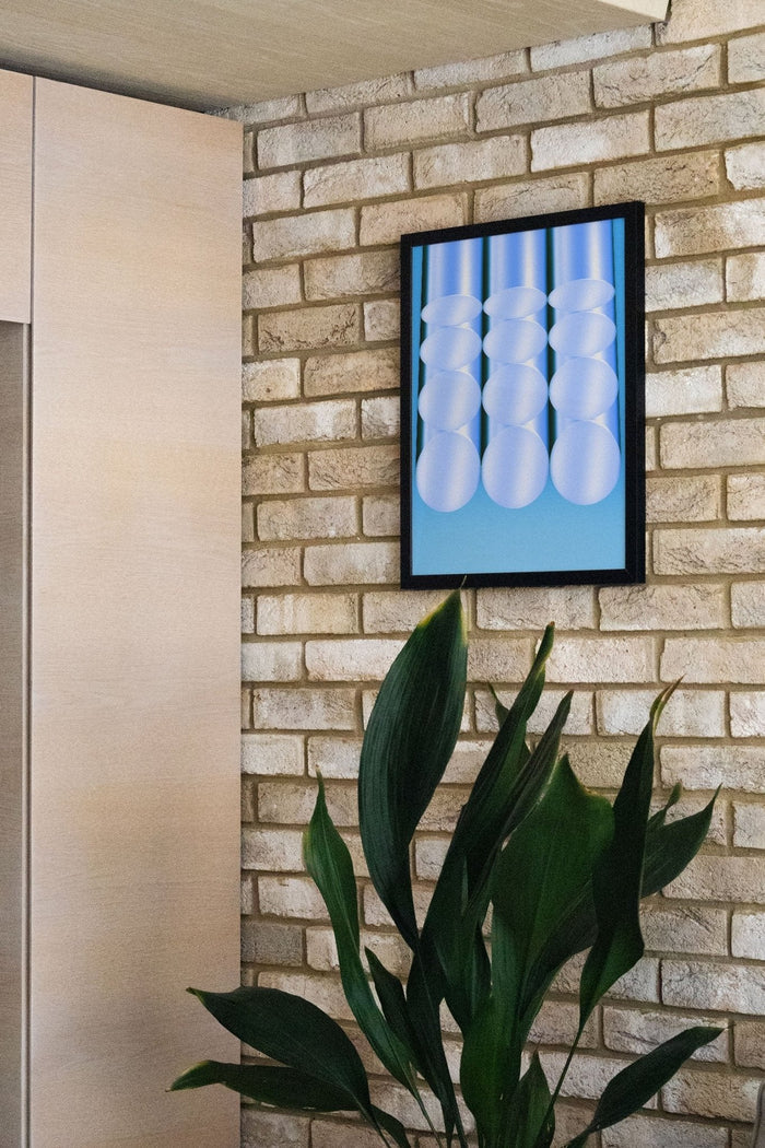 Tubes - Fergus Hannant artwork featuring abstract white tubes framed on a brick wall above green plants.